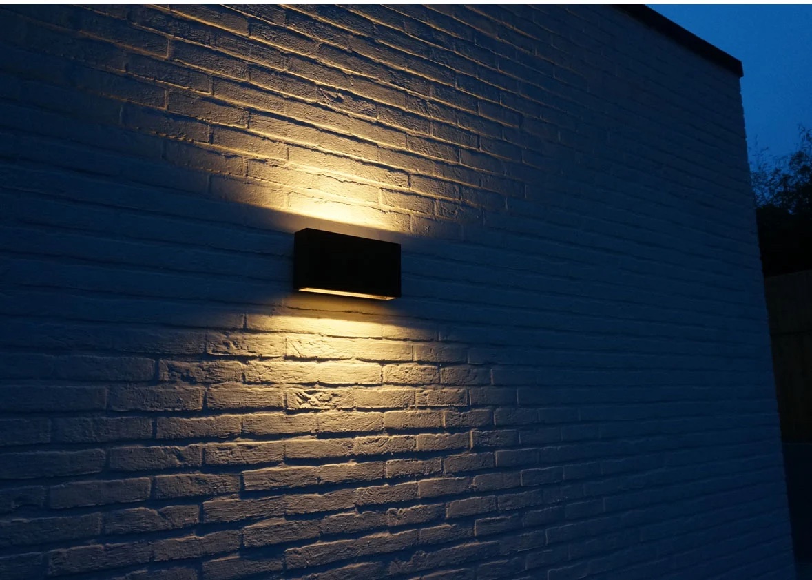 Außenwandleuchte Bronze mit warmweißem Up-Down-Licht an einer strukturierten Fassade